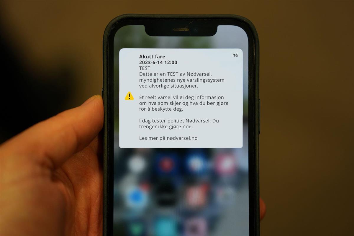 illustrasjonsbilde for nødvarsel hvor en hånd holder en telefon med nødvrasel fra myndighetene - Klikk for stort bilde